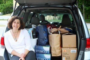 Laura Van Zandt, Executive Director of REACH Beyond Domestic Violence, poses with donations from a previous Shower for Shelters Collection.